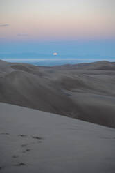 Moon dipping below mountains in sand dunes - CAVF74970