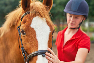 Teenage girl in equestrian helmet petting horse - CAIF24272