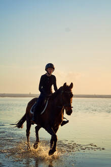 Young woman horseback riding in ocean surf - CAIF24276