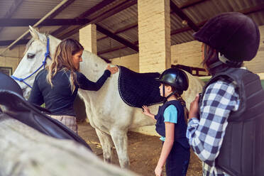 Female instructor helping girls prepare for horseback riding - CAIF24280