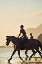 Junge Frau reitet am Strand bei Sonnenuntergang - CAIF24296