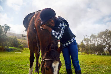 Glückliches Mädchen umarmt Pferd in ländlichem Gras Paddock - CAIF24302