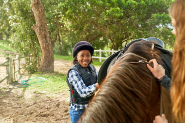 Portrait confident girl preparing saddle for horseback riding - CAIF24321