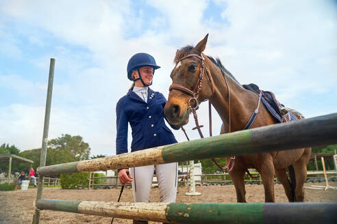 Teenage girl in equestrian helmet with horse at obstacle in paddock - CAIF24324