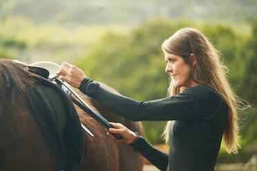 Woman preparing saddle for horseback riding - CAIF24339