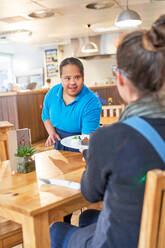 Junge Kellnerin mit Down-Syndrom serviert Essen in einem Cafe - CAIF24365