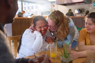 Fröhliche Mentorin und junge Frauen mit Down-Syndrom lachen im Cafe - CAIF24383