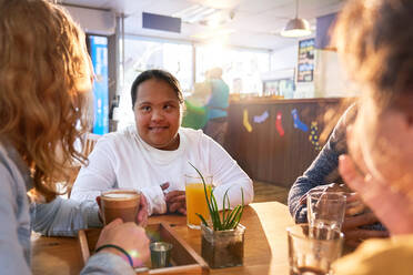 Smiling young woman with Down Syndrome talking with friends in cafe - CAIF24423