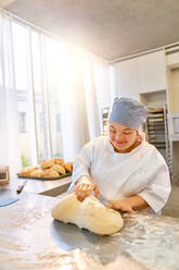 Smiling young woman with Down Syndrome kneading dough - CAIF24461