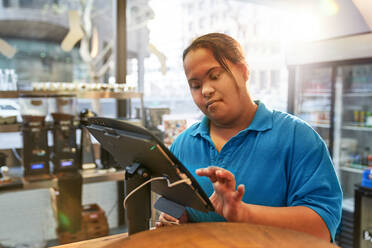 Junge Frau mit Down-Syndrom arbeitet an der Kasse eines Cafés - CAIF24473