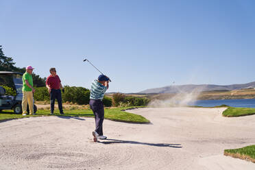 Mann, der aus einem Bunker auf einem sonnigen Golfplatz schießt - CAIF24476