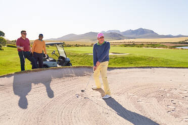 Älterer Mann schießt auf sonnigem Golfplatz aus dem Bunker - CAIF24482