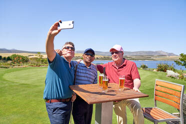 Männliche Freunde trinken Bier und machen ein Selfie auf der Terrasse des Golfplatzes - CAIF24484