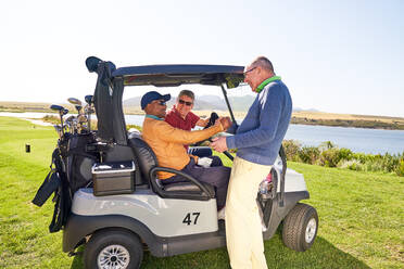 Männliche Golffreunde unterhalten sich am Golfwagen auf einem sonnigen Golfplatz - CAIF24492