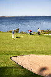 Männliche Golfer auf dem sonnigen Putting Green am Seeufer - CAIF24493
