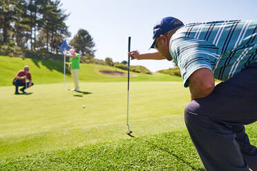 Männlicher Golfer bereitet sich auf dem sonnigen Golfplatz auf den Putt vor - CAIF24499
