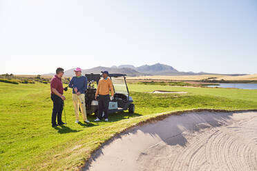 Männliche Golffreunde unterhalten sich im Sandloch auf einem sonnigen Golfplatz - CAIF24505