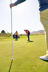 Männlicher Golfer, der auf einem sonnigen Golfplatz auf den Stift und das Loch zielt - CAIF24506