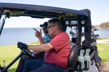 Männliche Golfer fahren Golfwagen auf einem Golfplatz am See - CAIF24507