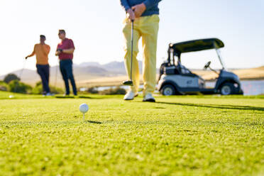 Male golfer preparing to tee off on sunny golf course - CAIF24509