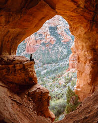 Woman sitting on edge of rock in cave, Sedona, Arizona, United States - ISF23801