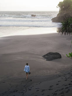 Junge Frau, die an einem felsigen Strand spazieren geht und die Aussicht betrachtet - CAVF74987