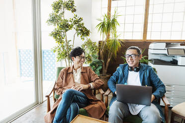 Zwei männliche japanische Fachkräfte arbeiten an Laptops in einem Co-Working Space. - MINF13749