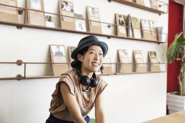 Eine japanische Berufstätige mit Trilby-Hut und Kopfhörern sitzt in einem Co-Working Space. - MINF13751