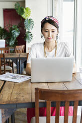 Eine japanische Berufstätige sitzt an einem Tisch in einem Co-Working Space und benutzt einen Laptop. - MINF13753