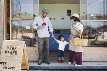 Japanischer Mann, Frau und Junge stehen vor einem Hofladen und halten sich an den Händen. - MINF13790