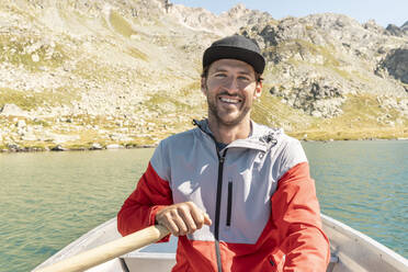 Junger lächelnder Mann in einem Ruderboot, Suretta-See, Graubünden, Schweiz - HBIF00032