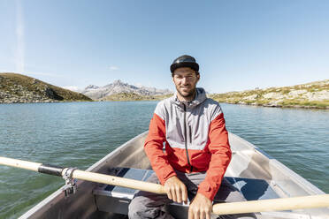 Junger lächelnder Mann in einem Ruderboot, Suretta-See, Graubünden, Schweiz - HBIF00034