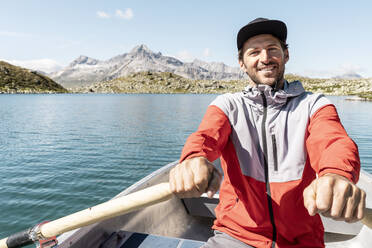 Junger lächelnder Mann in einem Ruderboot, Suretta-See, Graubünden, Schweiz - HBIF00035