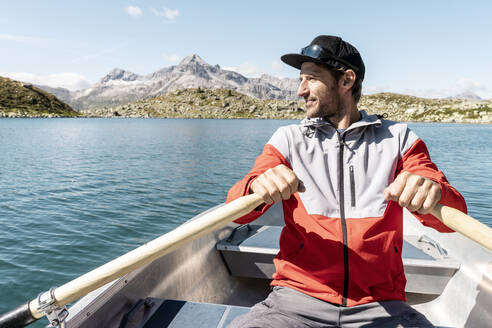 Junger lächelnder Mann in einem Ruderboot, Suretta-See, Graubünden, Schweiz - HBIF00036