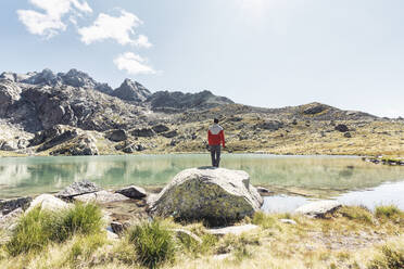 Rückansicht eines jungen Mannes auf einem Felsen mit Blick auf einen klaren Bergsee - HBIF00038