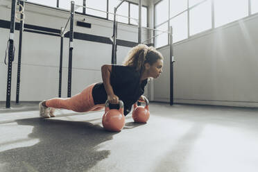 Junge Frau beim Training mit Kettlebells im Fitnessstudio - MTBF00345