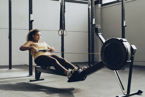 Junge Frau beim Training im Fitnessstudio mit Rudergerät, lizenzfreies Stockfoto