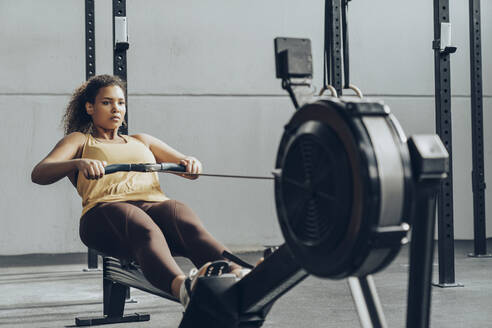 Young woman exercising in gym with rowing machine - MTBF00354