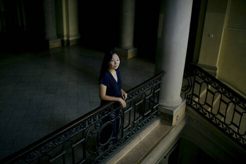 Portrait of serious woman leaning on banister in an old building looking at distance - OGF00148