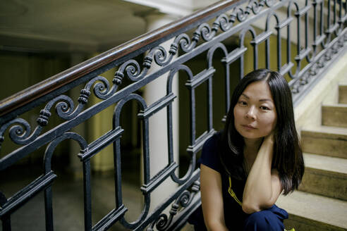 Porträt einer ernsten Frau, die auf einer Treppe in einem alten Gebäude sitzt - OGF00153