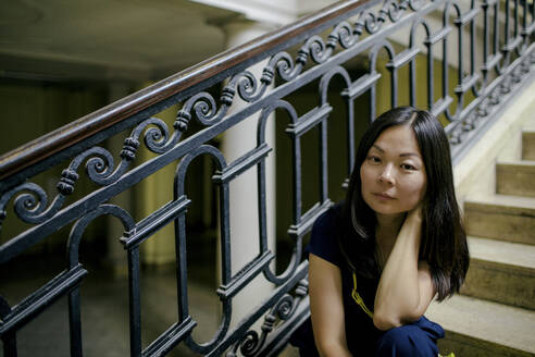 Portrait of serious woman sitting on stairs in an old building - OGF00153