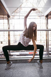 Young slim female in sports top and leggings standing barefoot on