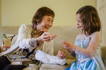 A smiling girl in princess costume opens up gift from her grandmother - CAVF75104