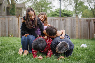 A laughing family pile up in a human pyramid in fenced in backyard - CAVF75105