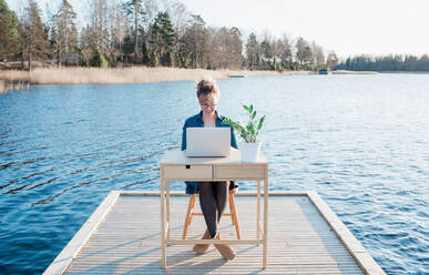 Frau arbeitet flexibel an einem Schreibtisch auf einer Seebrücke am Strand - CAVF75345