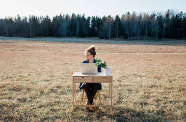 Reisende Frau arbeitet an einem Schreibtisch und Laptop in einem Feld bei Sonnenuntergang - CAVF75349