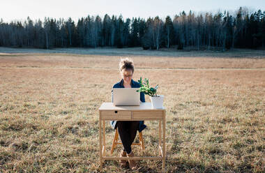 Reisende Frau arbeitet an einem Laptop und Schreibtisch in einem Feld im Freien - CAVF75350
