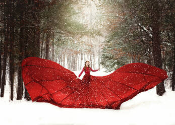 Young redhead girl in flowing red dress in forest with snowfall. stock photo