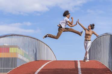 Man jumping mid air on bridge, highfiving woman - DLTSF00542