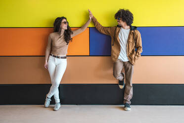 Smiling couple leaning against colorful wall, touching hands - DLTSF00545